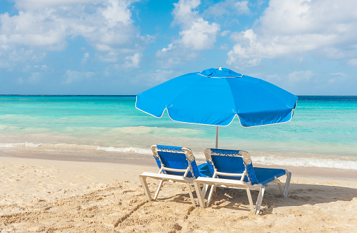 Blue set of two sunbeds and umbrella on a sandy beach near turquoise sea in Caribbean island of Barbados