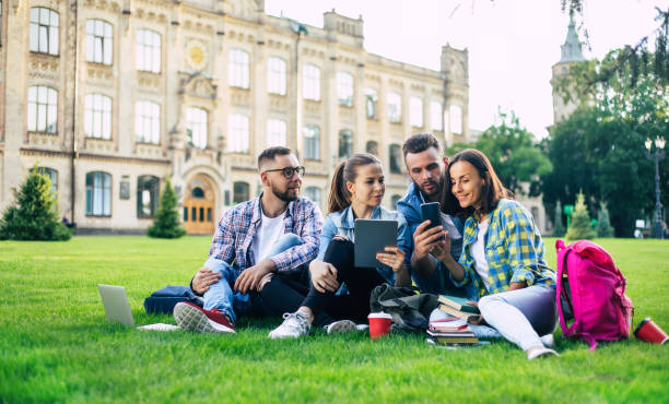 istock Happy beautiful students team with backpacks and other stuff are talking, having fun and relaxing on the grass on college background outdoors 1266795759