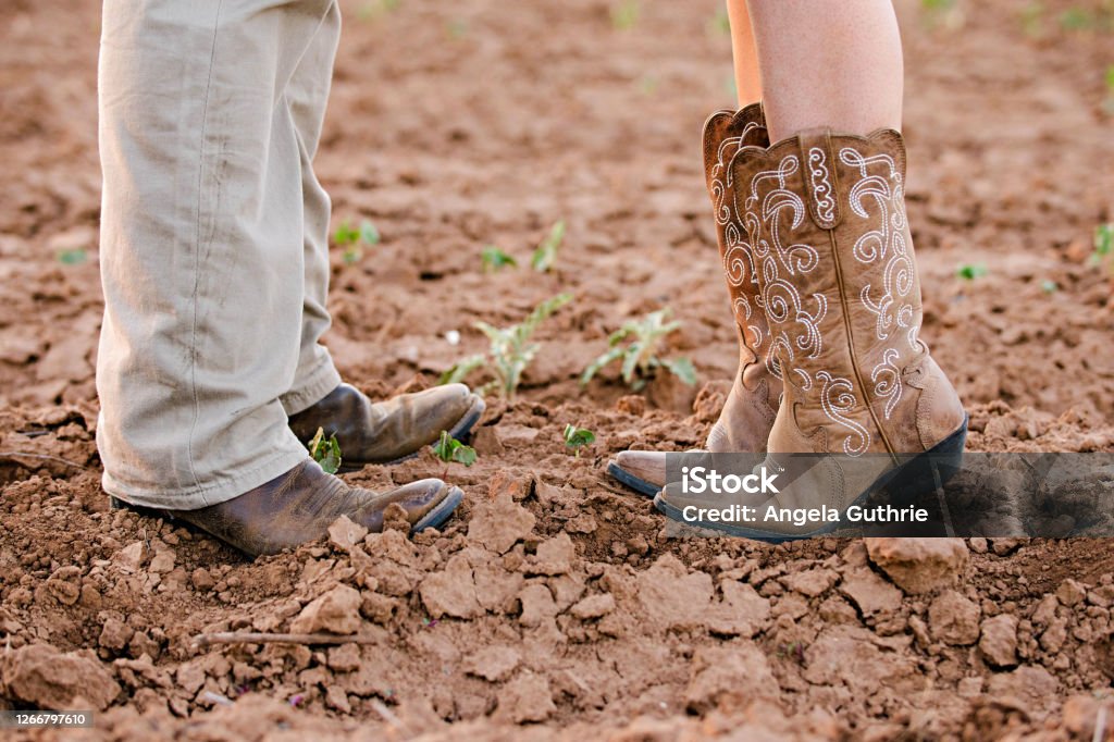 Couple wearing cowboy boots Male and female couple wearing cowboy boots in a dirt field. The woman is tiptoeing. Cowboy Boot Stock Photo