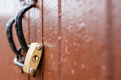 Shallow focus of a shackle type padlock seen looped to the doors of a wet garage, seen during a heavy downpour.