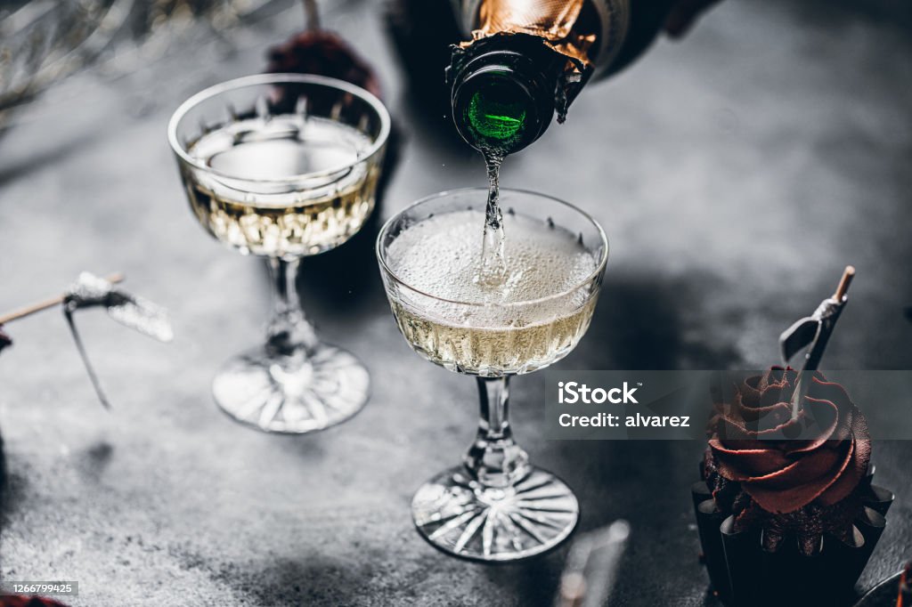 Serving drinks for new years party Close-up of pouring champagne in a glasses over black table with cup cake. Serving drinks for new years party. Champagne Stock Photo