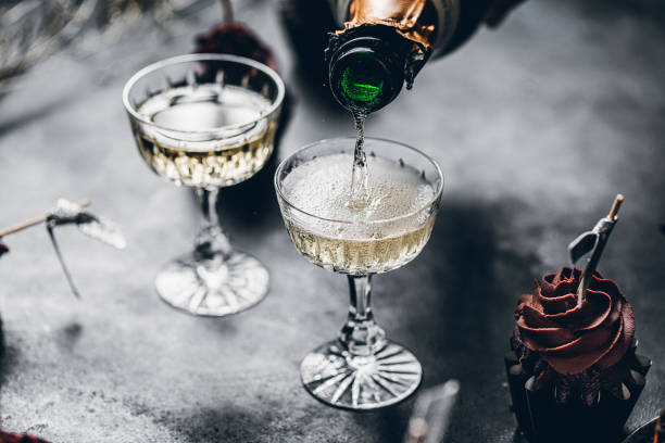 Serving drinks for new years party Close-up of pouring champagne in a glasses over black table with cup cake. Serving drinks for new years party. serving size photos stock pictures, royalty-free photos & images