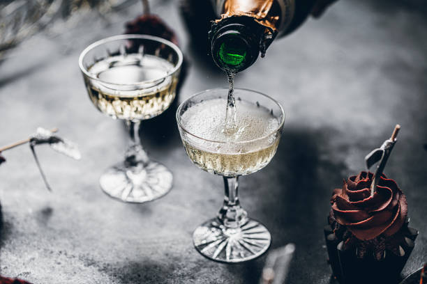 Serving drinks for new years party Close-up of pouring champagne in a glasses over black table with cup cake. Serving drinks for new years party. bottle empty nobody glass stock pictures, royalty-free photos & images