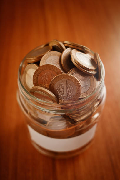 istock Coin savings jar with a blank label filled with cash on a table 1266802580