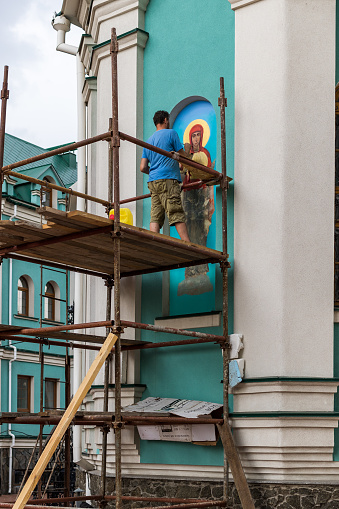 Kyiv, Ukraine - August 11, 2020: An unidentified Muralist repair a painting on the wall of an Orthodox church. Fresco painting on the outer wall of the Orthodox Church. Open air.