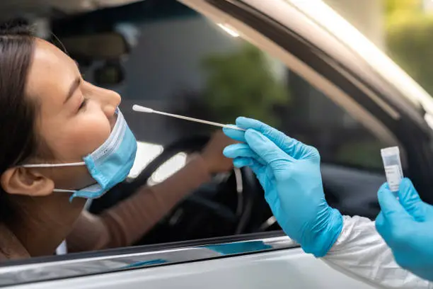 Portrait of asian woman drive thru coronavirus covid-19 test by medical staff with PPE suit by nose swab. New normal healthcare drive thru service and medical concept.