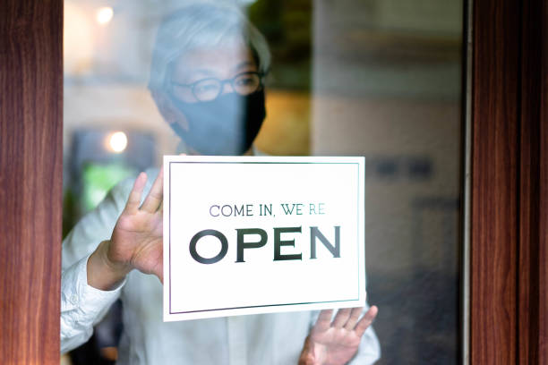 中年のアジア人男性が店頭に看板を掲げ、事業再開を発表する。 - store opening ストックフォトと画像