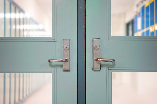 School closed due to Coronavirus. School closure under COVID-19 global pandemic. Selective focus on door and handle with blurred hallway, locker background. Fight against public health risk disease.