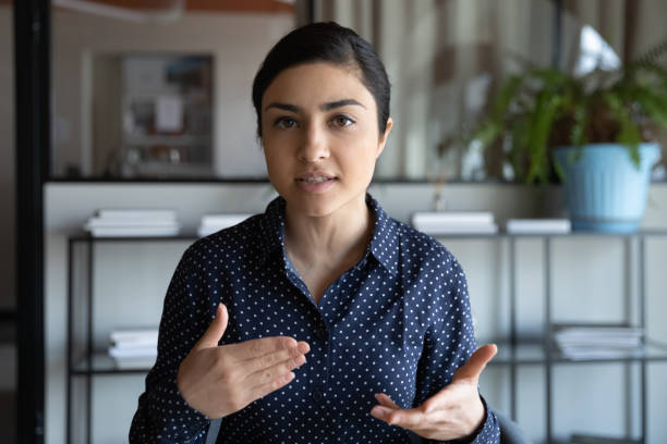 focused young indian woman holding negotiations video call with clients. - reduction looking at camera finance business imagens e fotografias de stock