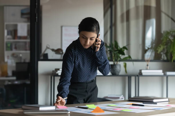 istock Concentrated serious young indian female employee holding call with client. 1266809665