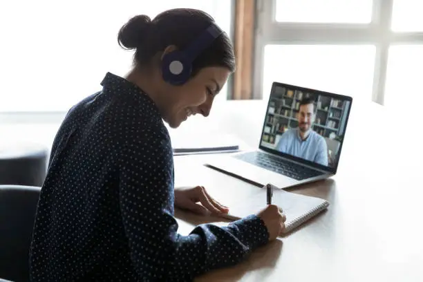 Photo of Happy mixed race girl listening to educational webinar, writing notes.