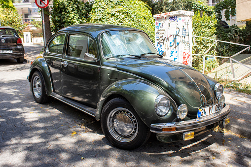 Bangkok, Thailand - February 15, 2014: Thai people are standing between many VW Beetle oldtimers on Siam VW festival of private owners. A group of men is watching a beetle with rusty styled chaissis and open top.