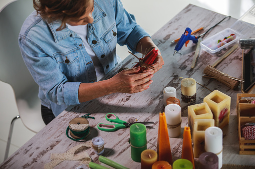 High angle view of artistic mature woman concentrating while crafting decorations for candles in her art studio as a hobby.