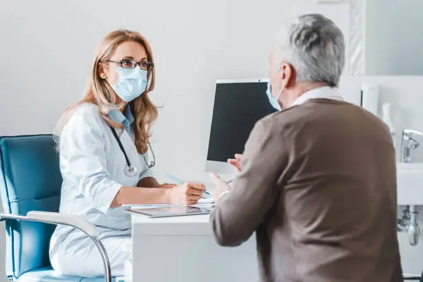 Woman doctor wear protection face mask talking with patient in clinic office