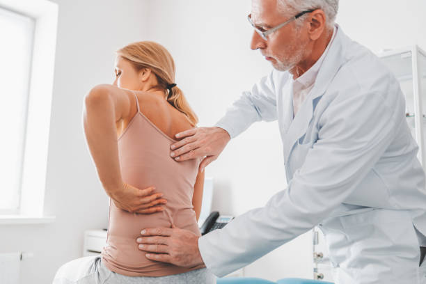 Senior male orthopedist examining patient's back in clinic Senior male orthopedist examining patient's back in clinic orthopedist stock pictures, royalty-free photos & images