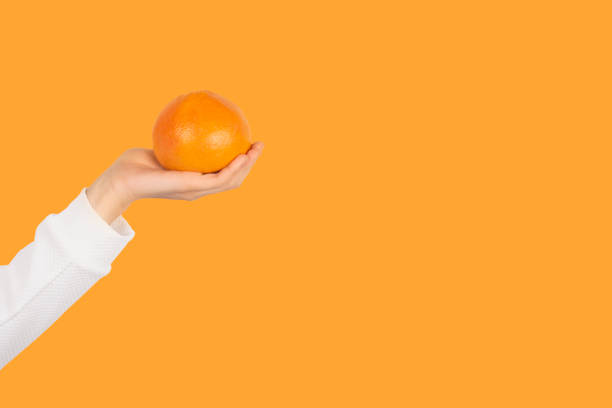 istock Female hand hold orange fruit isolated on orange background. 1266813515