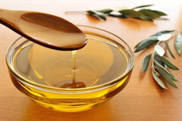 Pouring olive oil Pouring olive oil from wooden spoon to the bowl with olive branches beside the bowl. photo isolate on wooden background front view olive oil pouring antioxidant liquid stock pictures, royalty-free photos & images