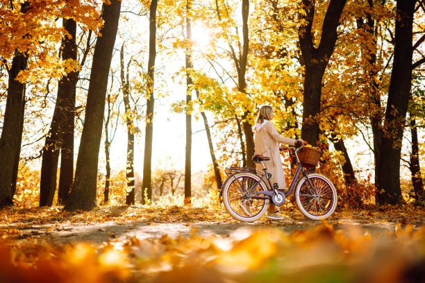 stylish woman with a bicycle enjoying autumn weather in the park. - autumn sun oak tree imagens e fotografias de stock