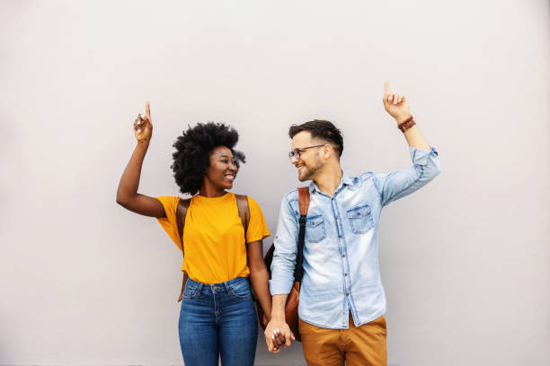 istock Young attractive multicultural hipster couple holding hands and pointing up. 1266817896