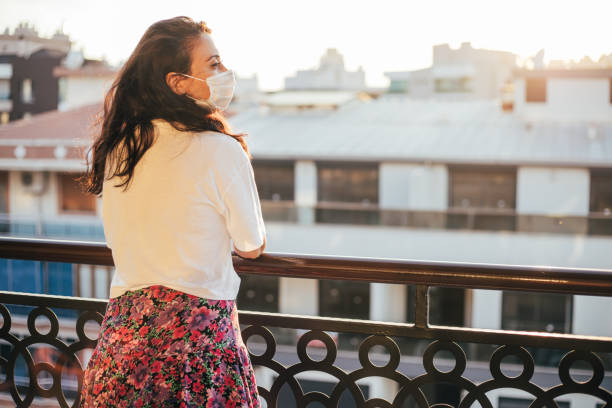 istock Woman wearing protective face mask admiring sunset from her balcony 1266818277
