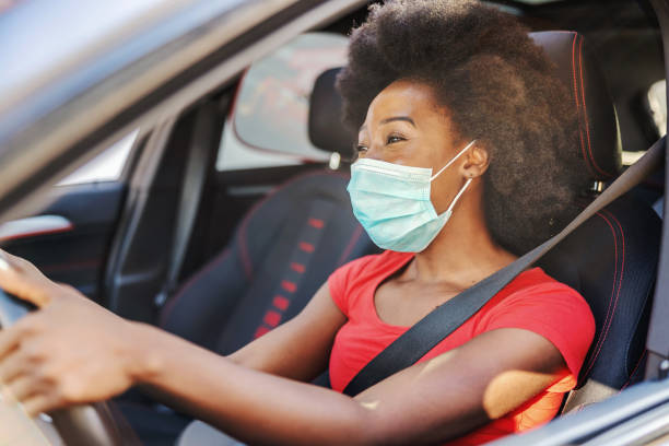 young attractive african woman with mask on her face driving her car during covid-19 pandemic. - illness mask pollution car imagens e fotografias de stock