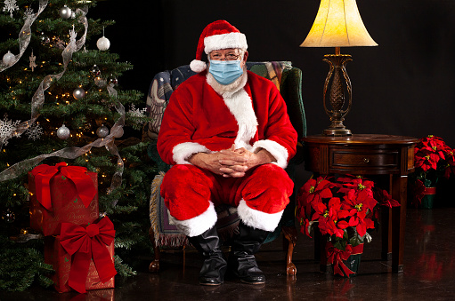 Santa Claus Sentado en una silla Usando una Máscara Quirúrgica y Mirando Hacia la Cámara photo