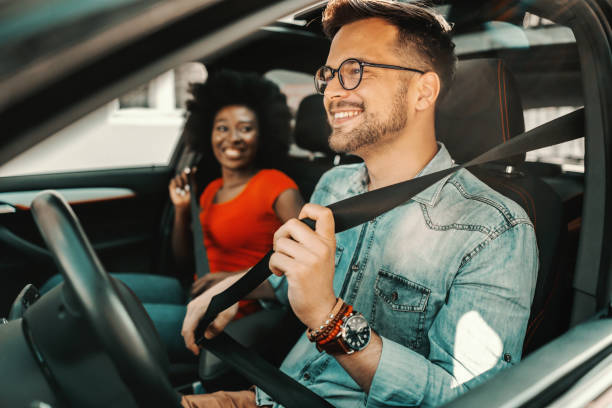 joven pareja multirracial sentada en un coche y abrochando cinturones de seguridad. - volante fotografías e imágenes de stock