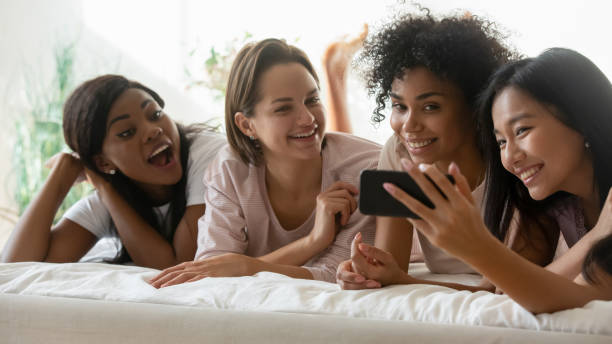 istock Multiracial girls enjoy time together lying in bed using smartphone 1266822031