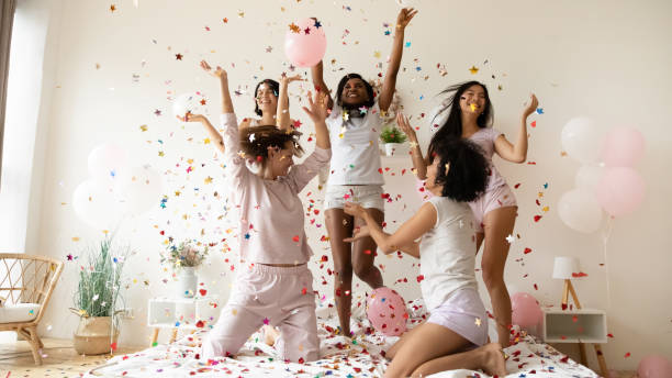 istock Multiethnic women wearing pyjamas dancing on bed under falling confetti 1266822059