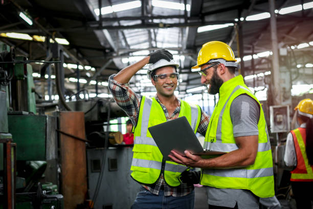 istock Industrial engineer wearing helmet and safe glasses, holding laptop computer for operating machinery at manufacturing plant factory, worker team working together in industry concept 1266824347