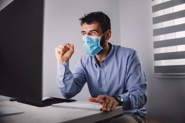 istock Young attractive programmer with face mask on sitting in his office and celebrating success during corona virus outbreak. 1266825647