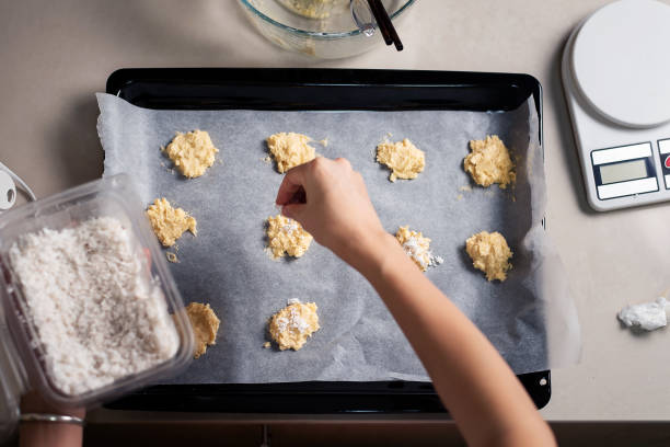 женщина организации кокосовое печенье тесто на сковороде, покрытой бумагой для выпечки на кухне дома крупным планом - baking paper cookie tray стоковые фото и изображения