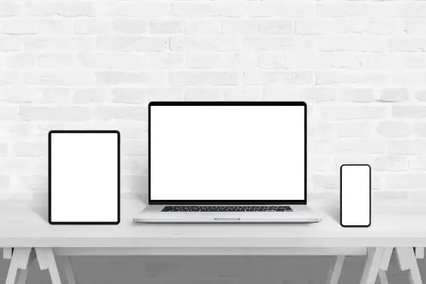 Photo of Devices with isolated screens for responsive web design promotion. Web design studio concept on white wooden desk and brick wall in background