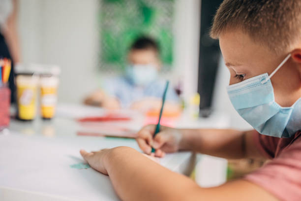 istock Young preschool boy with protective face masks drawing in class 1266828356