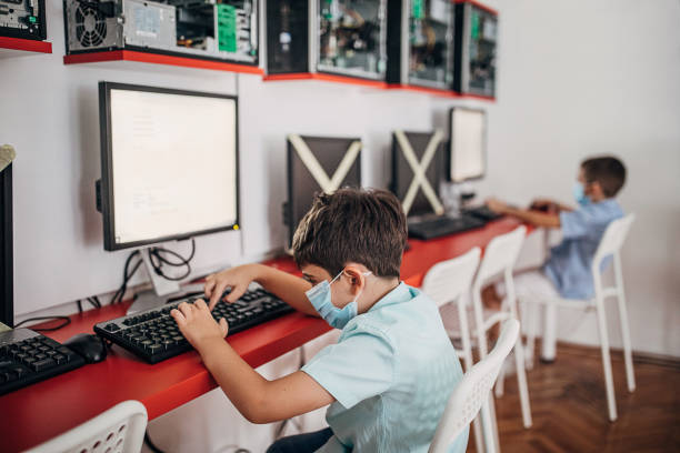 jóvenes escolares que usan máscaras protectoras en el aula de computación - computer lab child internet development fotografías e imágenes de stock