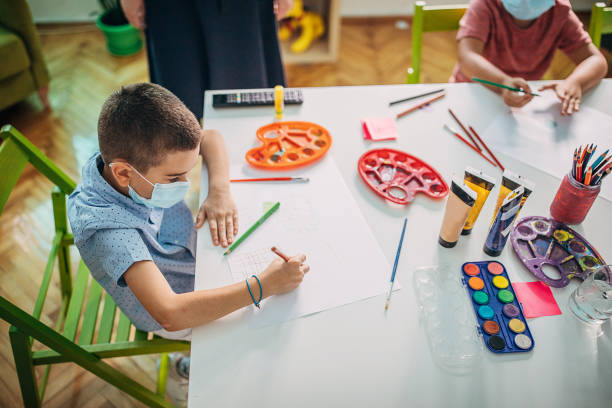 istock Preschool boy with protective face masks drawing in class 1266830775