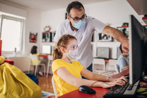 estudiantes en edad preescolar y profesor que usan máscaras protectoras en el aula - computer lab child internet development fotografías e imágenes de stock