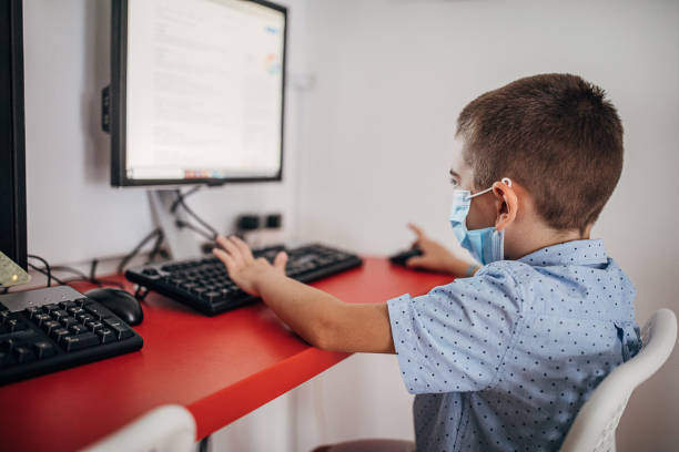 chłopiec w wieku przedszkolnym noszący ochronną maskę na twarz w klasie komputerowej - computer lab child internet development zdjęcia i obrazy z banku zdjęć