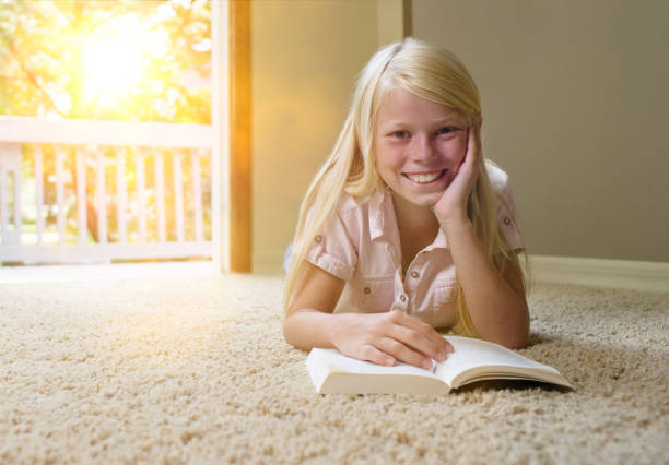 istock Girl lying on carpet, reading book 1266832100