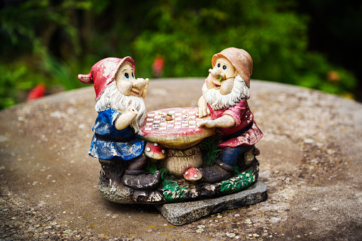 Two garden gnomes sit on a stone and play chess