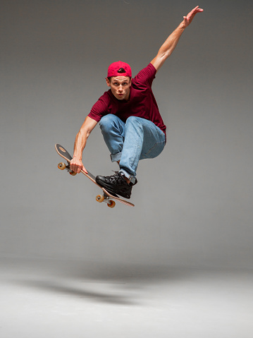 Cool young guy skateboarder jumps on skateboard in studio on gray background. Photography about skateboarding tricks. High quality photo