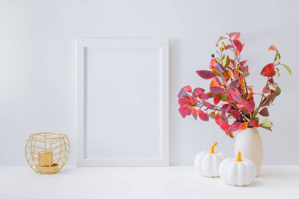 istock Home interior with decor elements. Mockup with a white frame, colorful autumn leaves in a vase on a light background 1266833407