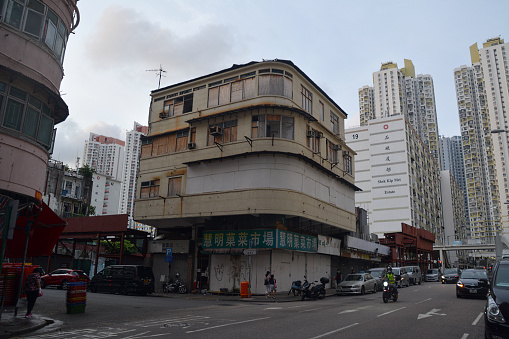 Intersection by a traditional Tong Lau architecture apartment building in Mongkok, Hong Kong. People walking on the sidewalks.