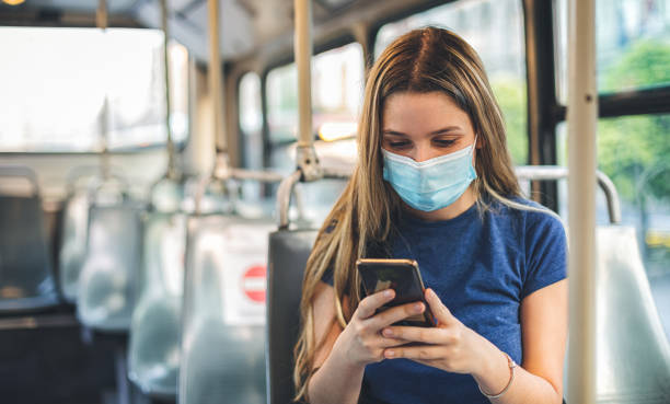 istock Student girl using smart phone while sitting in a bus. She's wearing a protective face mask to protect from coronavirus COVID-19. Back to school concept 1266837710