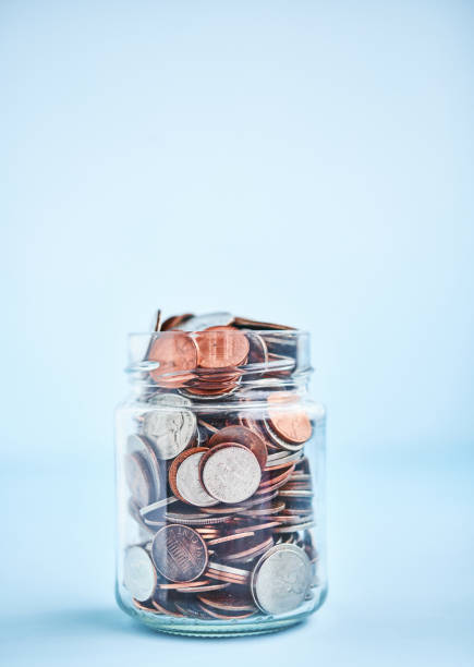istock Loose Change Jar Filled with Coins on Bright Blue Background 1266838111