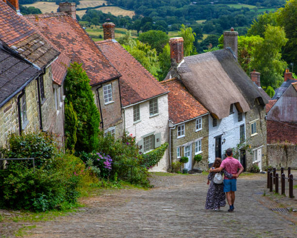 Gold Hill in Shaftesbury, Dorset, UK A couple enjoying the picturesque Gold Hill in the town of Shaftesbury in Dorset, UK.  The hill was made famous by being in the iconic Hovis advert. shaftesbury england stock pictures, royalty-free photos & images