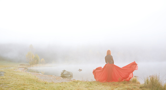 Rear view of woman wearing red skirt posing in fairytale concept, standing in front of lake