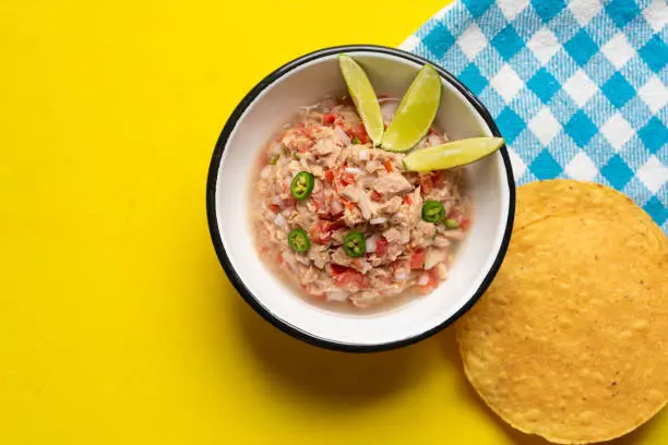 Fresh canned tuna ceviche with chili pepper and tomato on yellow background