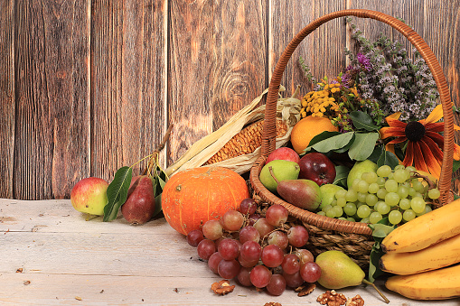 A Thanksgiving cornucopia of fruits and vegetables rests on a table in front of an old world painted background.