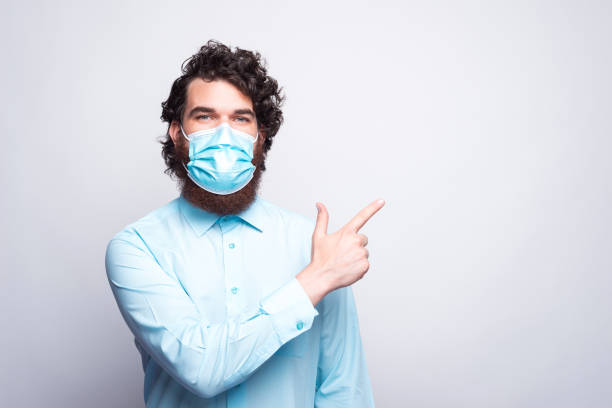 istock Man wearing medicinal facial mask and pointing at copyspace 1266847739